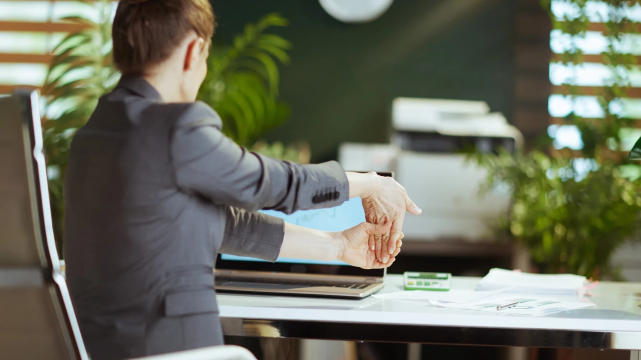 Sustainable workplace. Seen from behind modern business woman in a grey business suit in modern green office stretching hand.